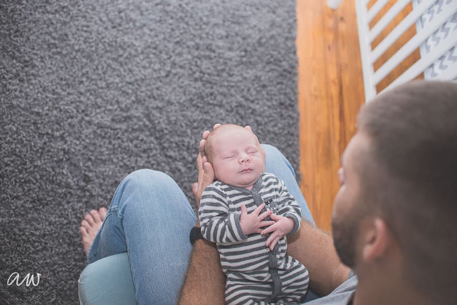 a newborn son resting on his daddy's legs in their nursery