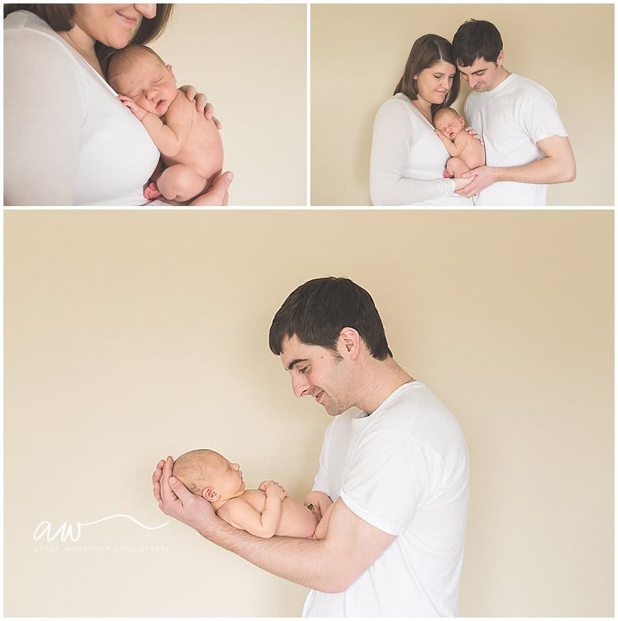 Mom and dad holding baby in front of a white wall.