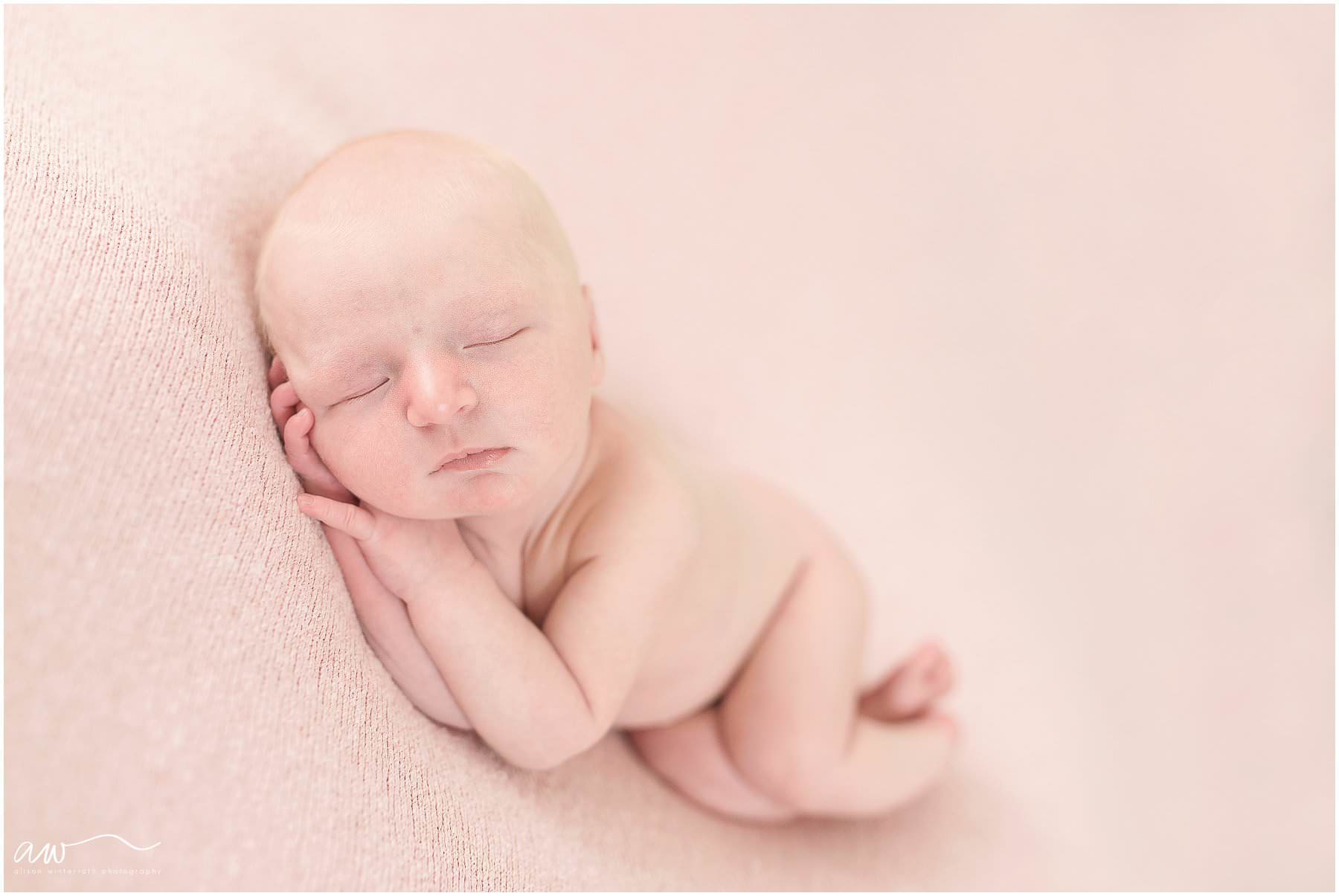 newborn baby on pink fabric sleeping.