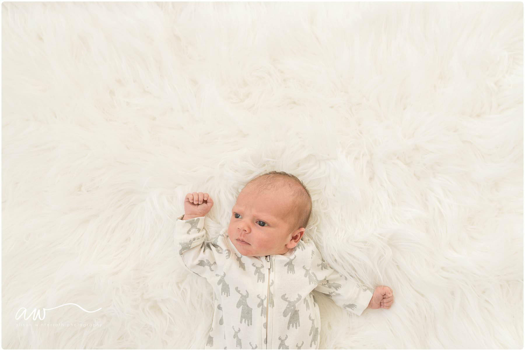 A newborn baby looks around on a white fur blanket