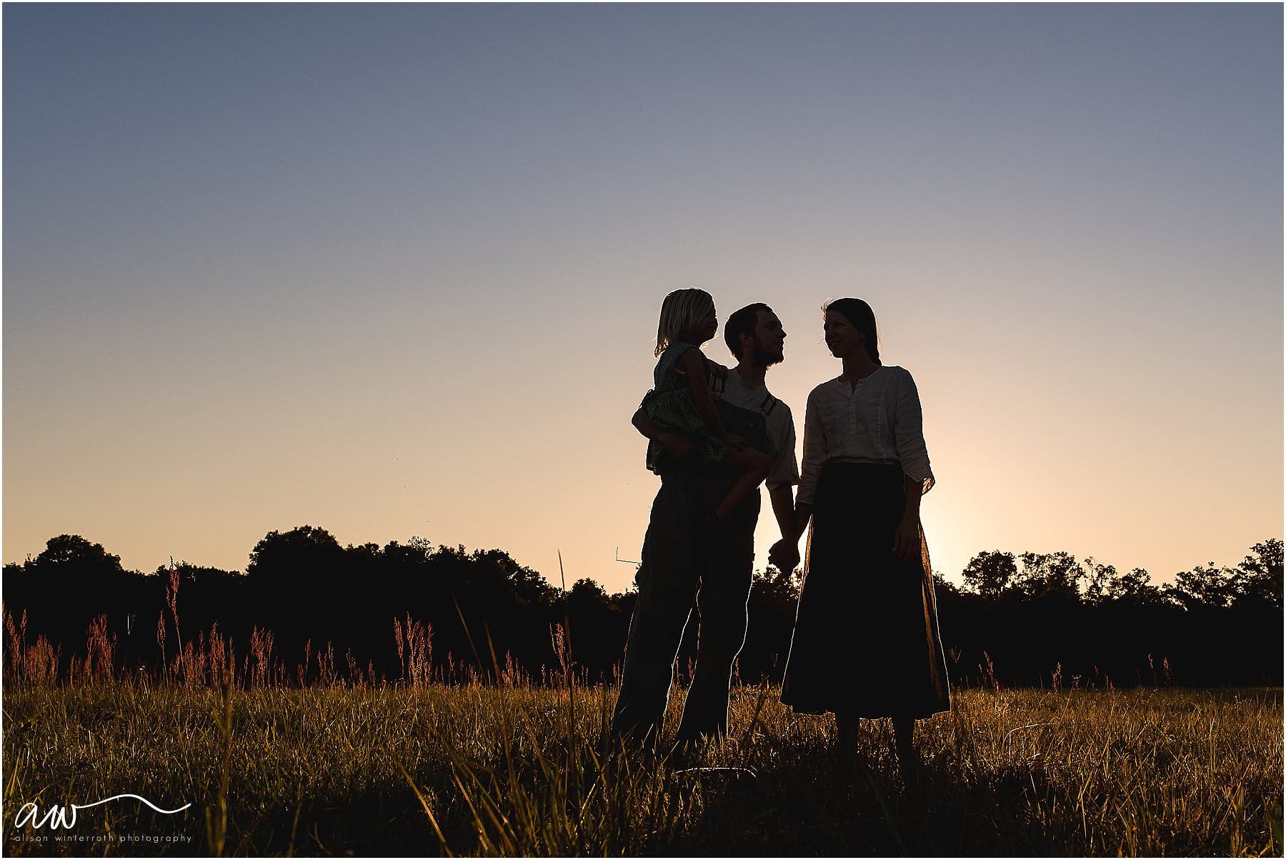 Family of three silhouetted to the sky at sunset