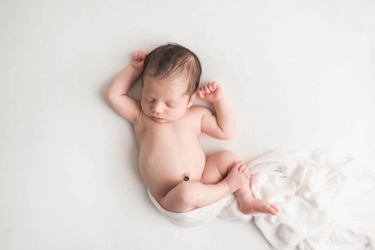 A tiny newborn baby on a white blanket sleeping sweetly