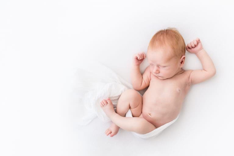 a redheaded newborn sleeping on a white bed
