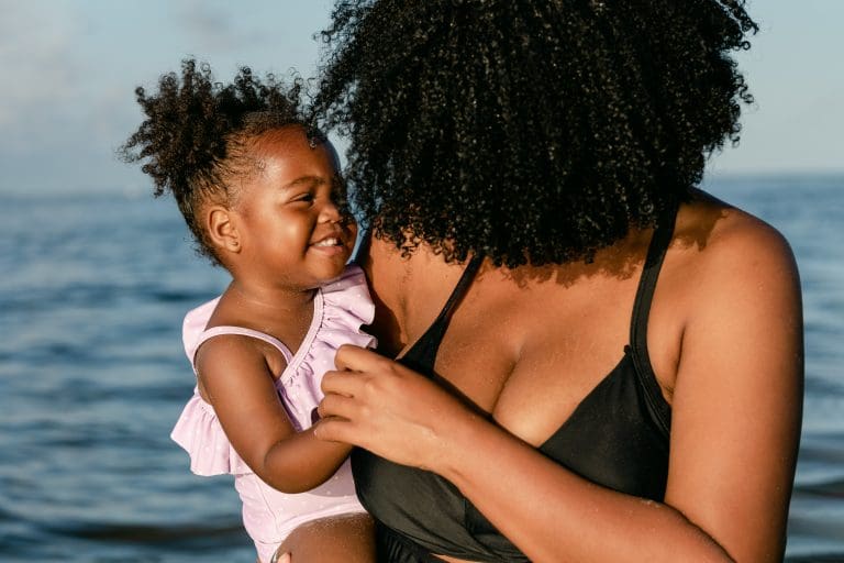 Mom with curly hair smiling at her daughter at the beach