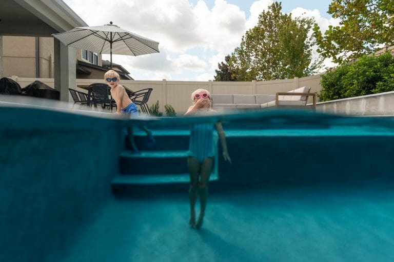 girl holding her nose underwater as her brother watches