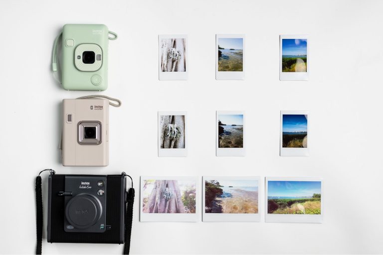three hybrid cameras in a row with three prints lined up next to them on a white surface.